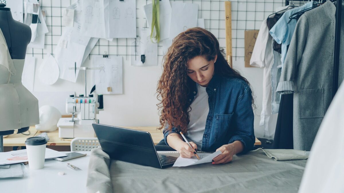 Patroană a unui atelier de croitorie care își notează serviciile și prețurile lângă laptop, informațiile din care asistentul AI știe ce să răspundă