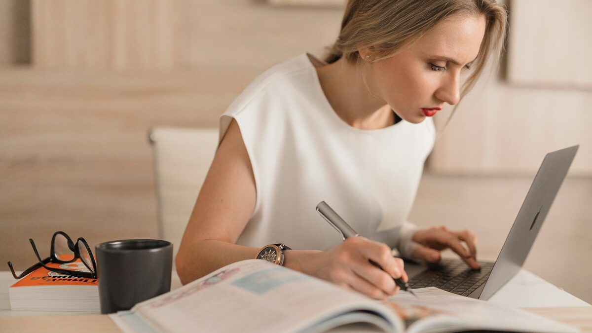 Freelanceră care calculează în caiet și pe laptop prețul pentru un proiect freelance