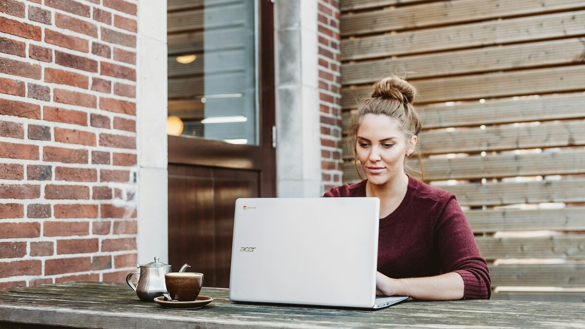 Freelanceră la o terasă de cafenea care își caută primii clienți fără platforme, scriind mesaje pe laptop
