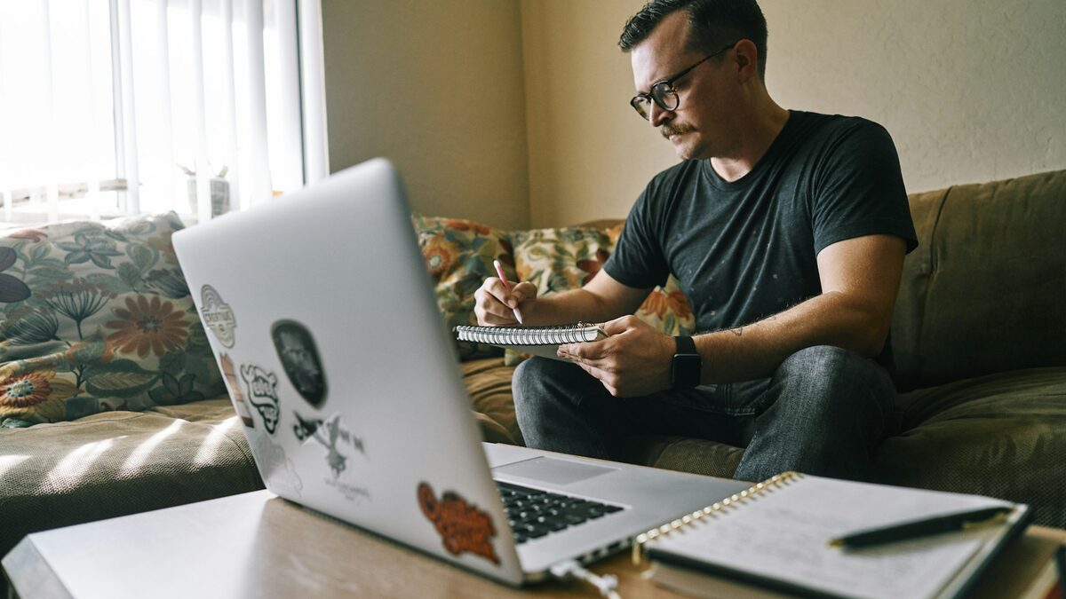 Freelancer pe canapea care scrie propunerea pentru un client nou, cu notițele alături de laptop