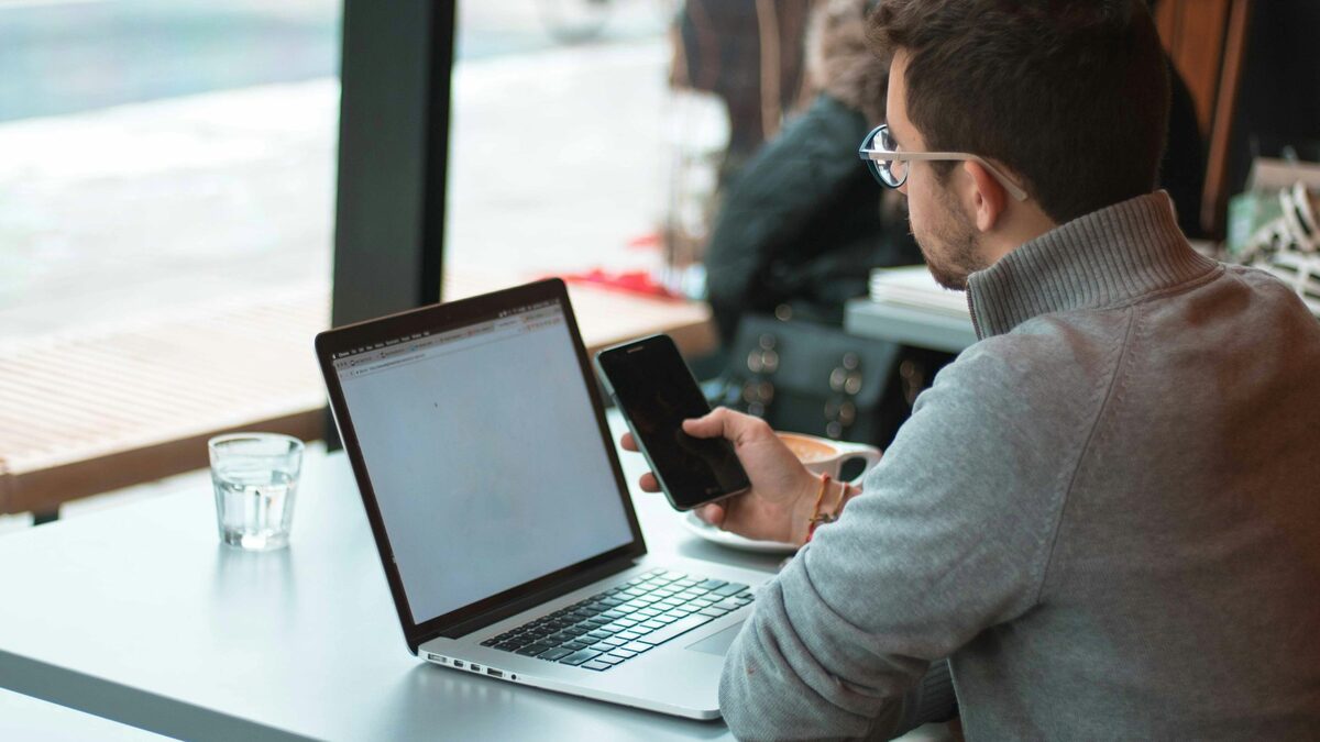 Tânăr la laptop, lângă fereastră, care își completează profilul pe Upwork, Fiverr și alte platforme