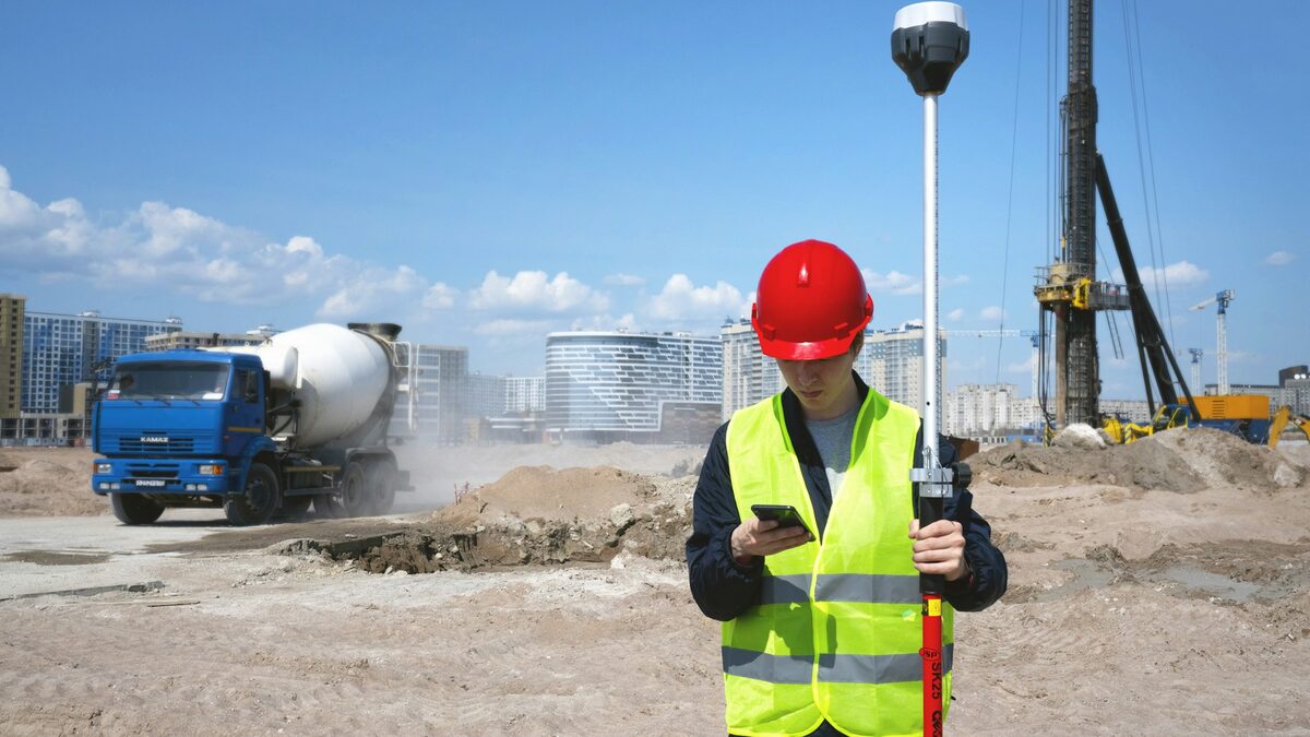 Muncitor cu cască și vestă reflectorizantă pe șantier, care exersează pe telefon limba germană pentru construcții