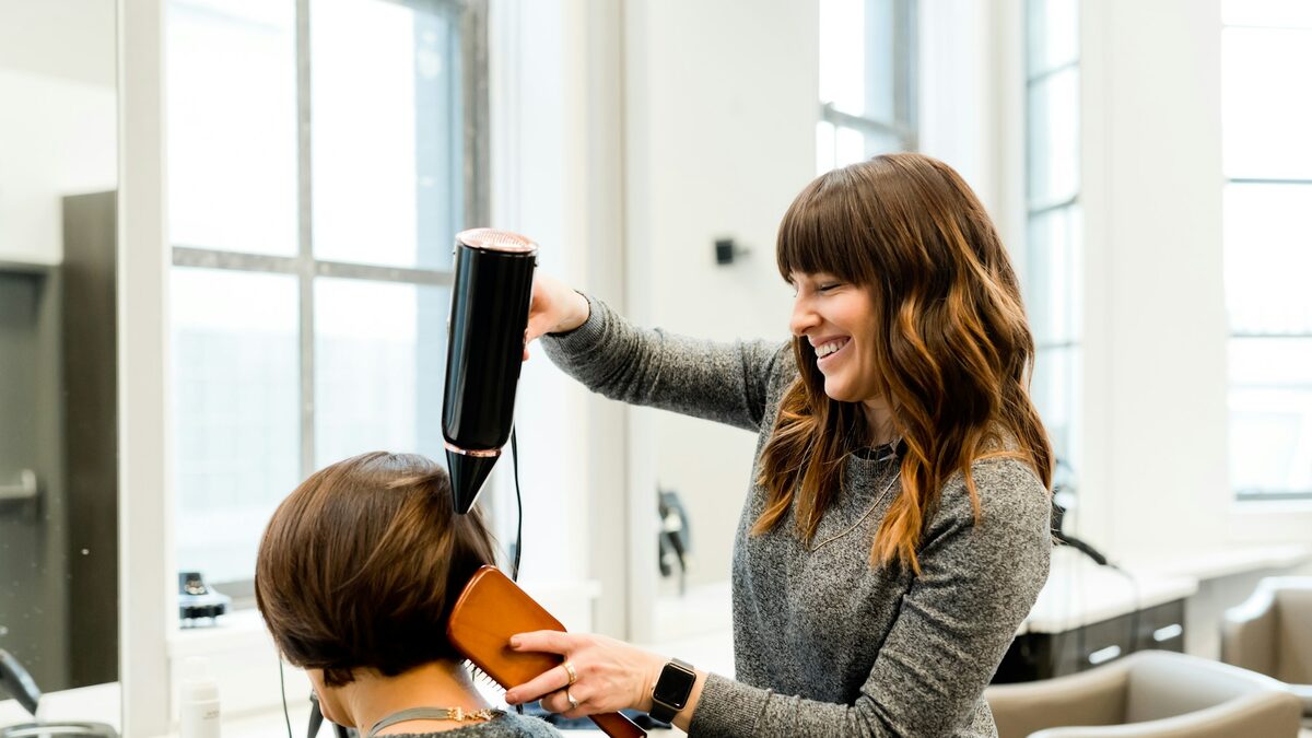 Hairstilistă zâmbitoare care coafează o clientă într-un salon de înfrumusețare luminos