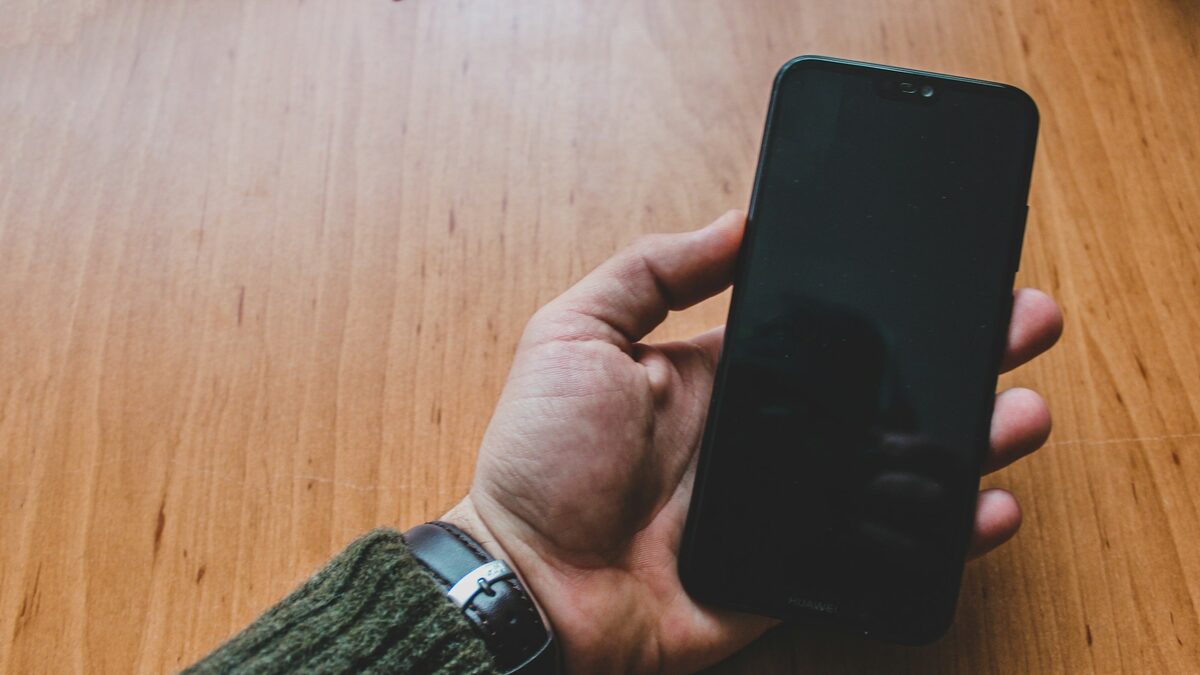 Mână care ține un iPhone deasupra unei mese de lemn, gata pentru configurarea Apple Intelligence