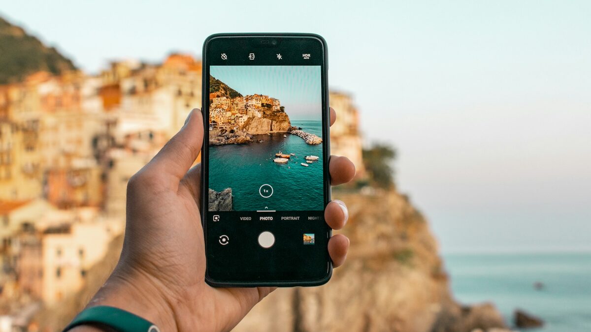 Mână care fotografiază cu telefonul un peisaj de vacanță, înainte de editarea pozelor cu AI pe telefon