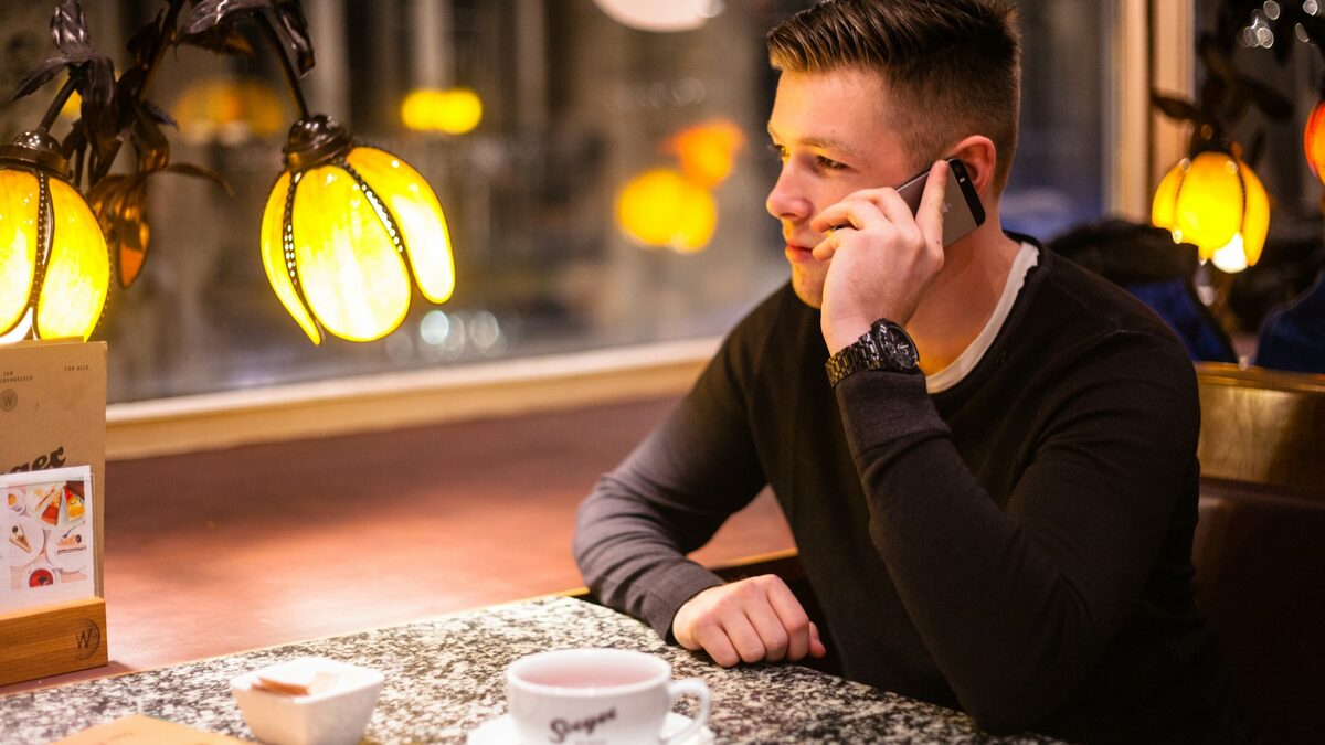 Bărbat într-o cafenea care folosește traducerea apelurilor pe telefon, vorbind cu un proprietar din străinătate