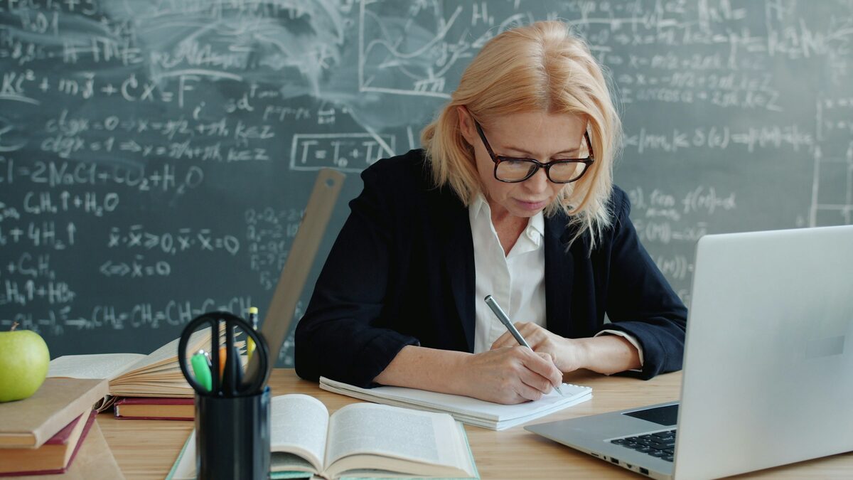 Profesoară la catedră care lucrează la planificarea calendaristică cu AI pe laptop, cu notițele și manualele alături
