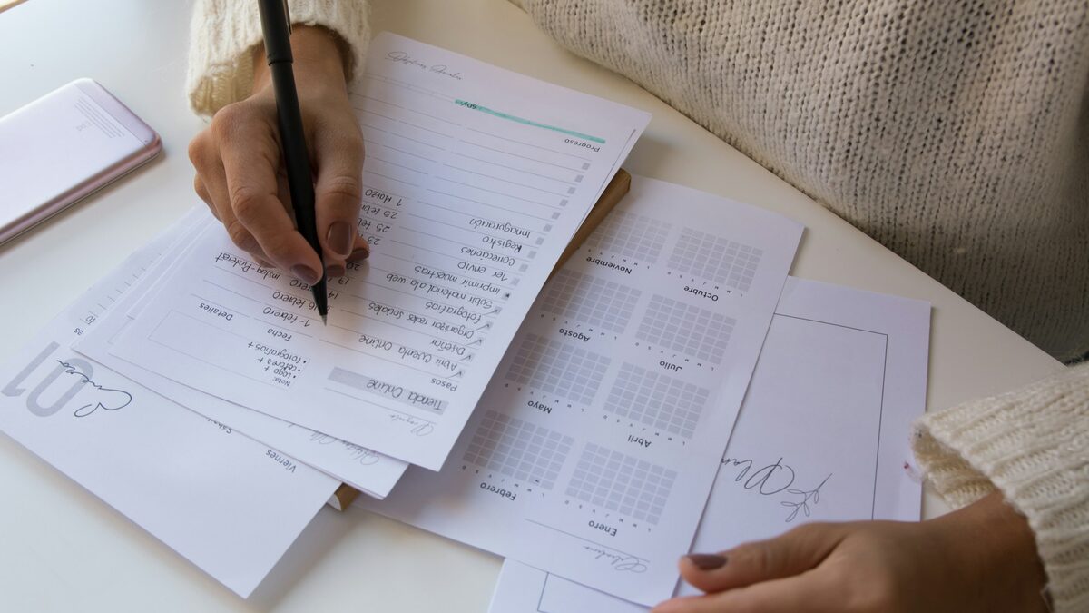 Mână care corectează cu creionul testele de evaluare create cu AI și tipărite pentru clasă