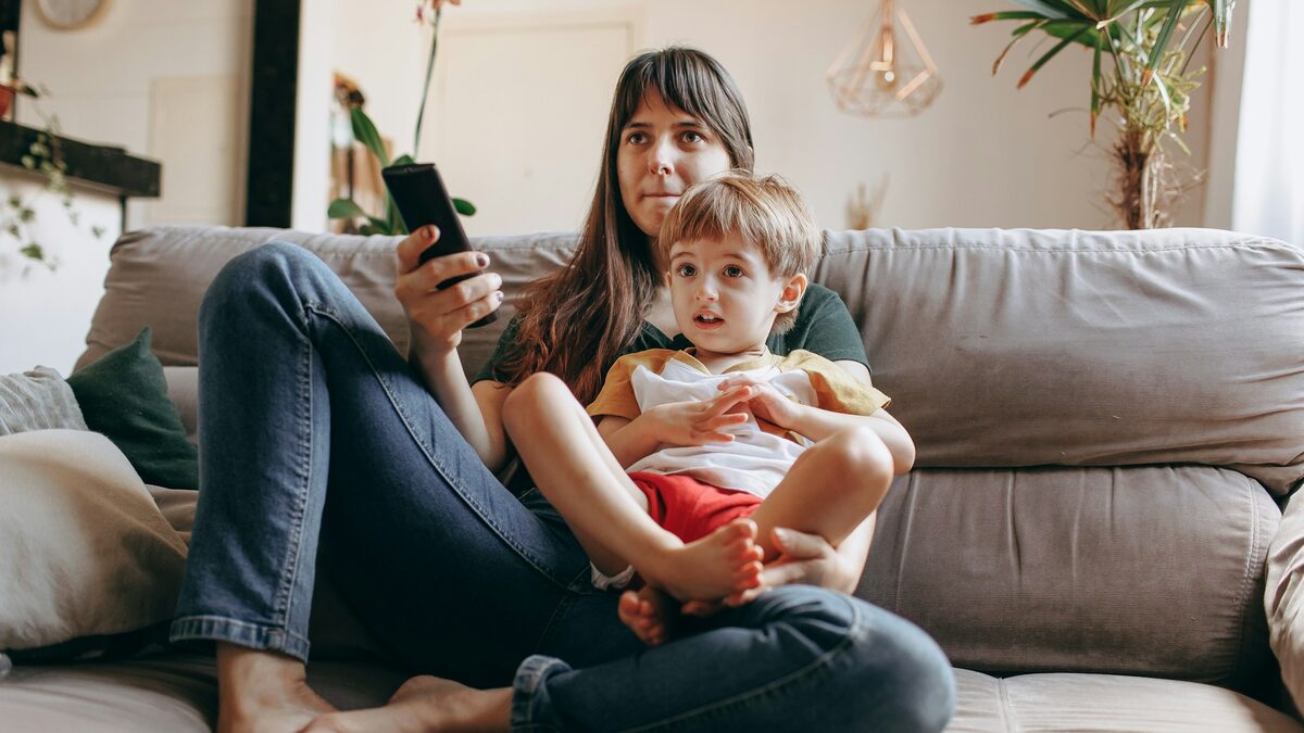Mamă pe canapea, cu copilul în brațe, care își notează pe telefon întrebările părinților la pediatru