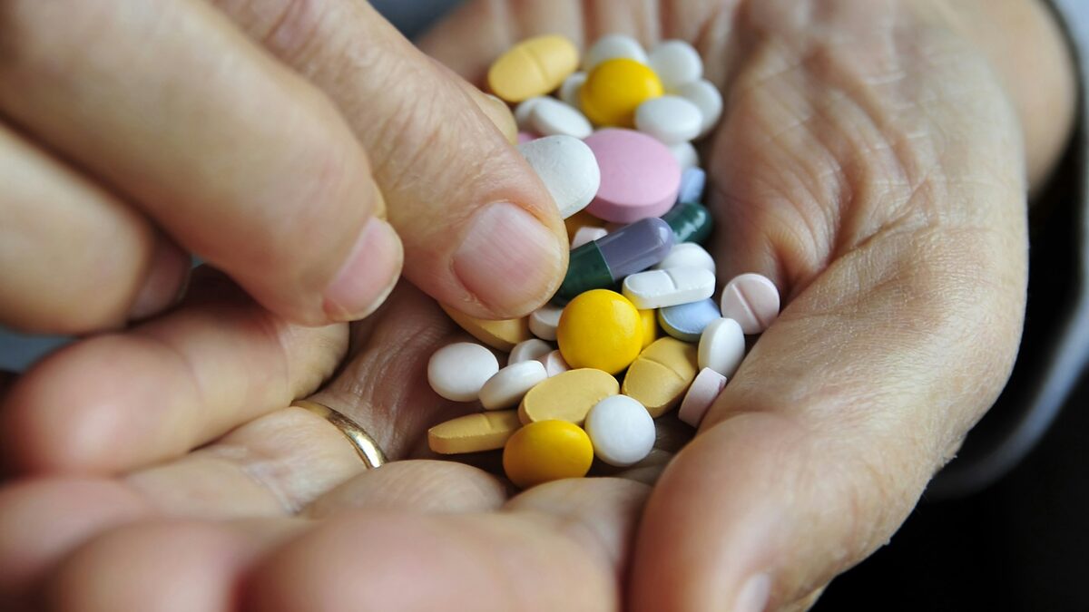 Pastile colorate în palma unei vârstnice; un memento pentru medicamente pe telefon ajută la ora potrivită