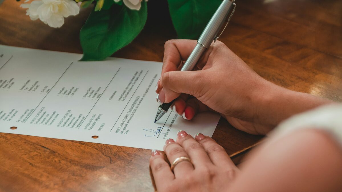 Mână care semnează un document pe birou, după ce a citit ce trebuie să scrie în oferta pentru site