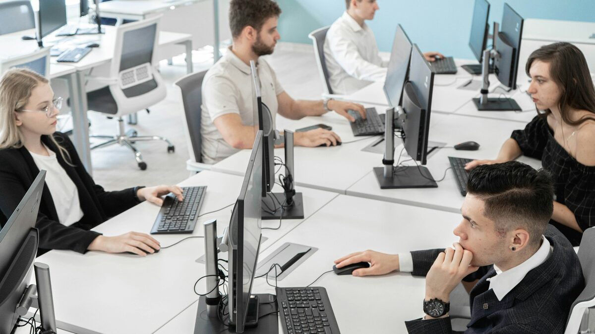 Colegi care lucrează la calculatoare într-un birou, unde programele firmei trebuie să comunice între ele