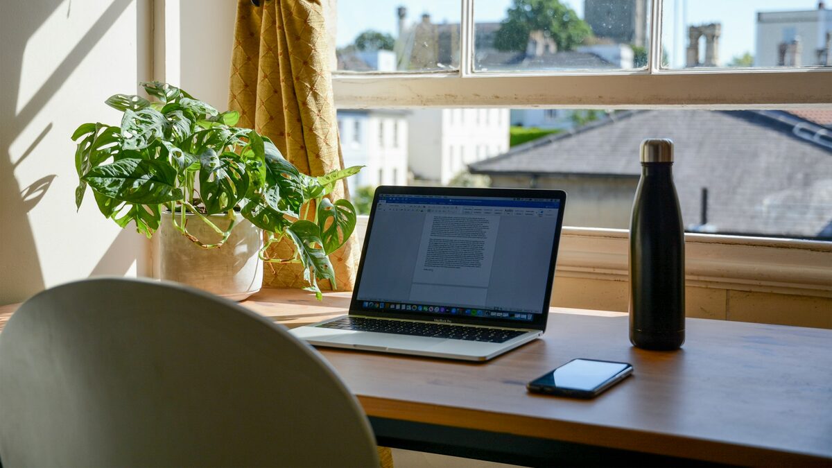 Laptop deschis pe un birou luminos lângă fereastră, pregătit pentru lucrul cu Microsoft Copilot