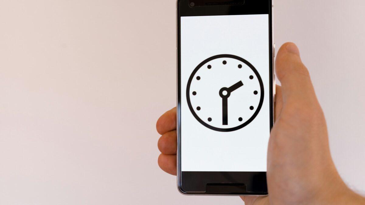 Mână care ține un telefon cu un ceas pe ecran, ca reamintire prin care reduci programările uitate