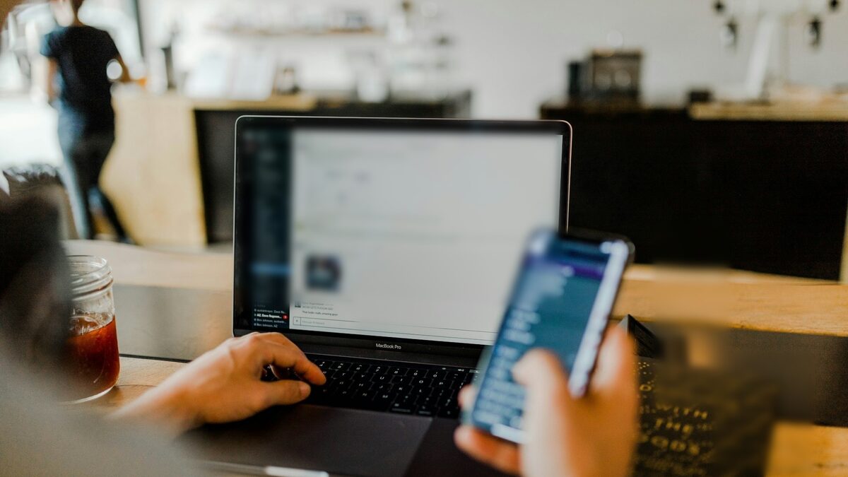 Mâini care lucrează la laptop și pe telefon, cu mesajele din toate canalele într-un singur loc