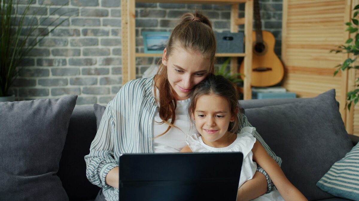 Mamă și fiică pe canapea, folosind împreună laptopul, un moment din relația dintre copiii și ChatGPT