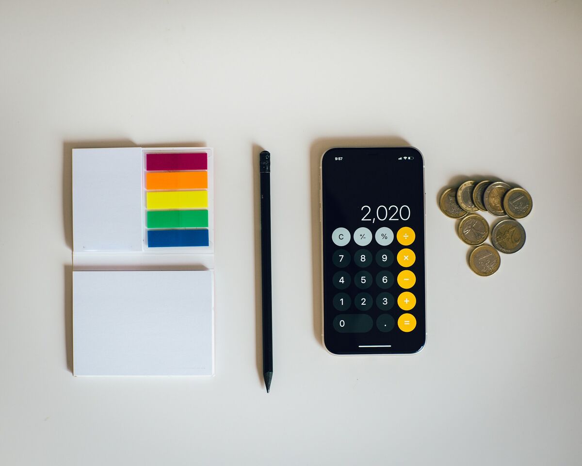 Calculator pe telefon, monede și notițe pe birou, pentru socoteala costurilor anuale ale unui site