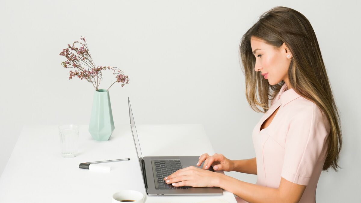 Femeie la laptop care scrie cu atenție descrierea pentru imagini AI, într-un birou luminos