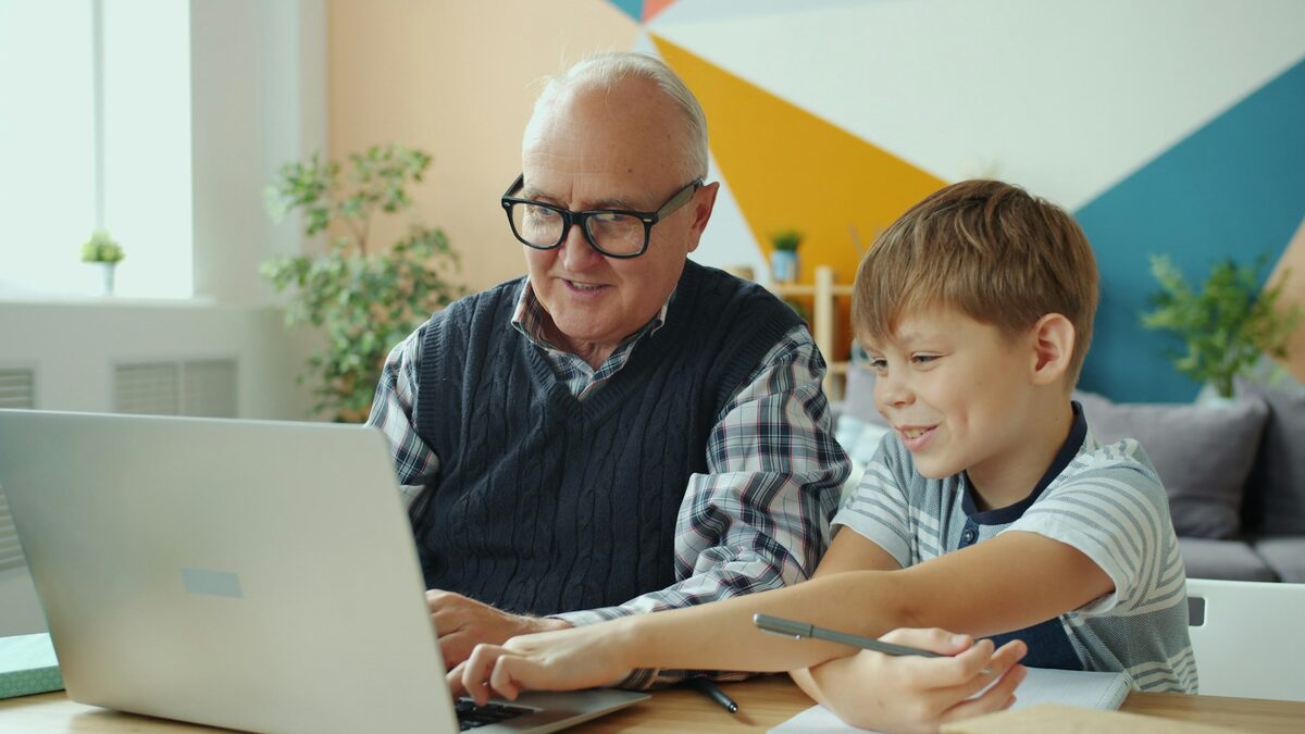 Bunic și nepot la masă, cu un laptop deschis, discutând ce este inteligența artificială