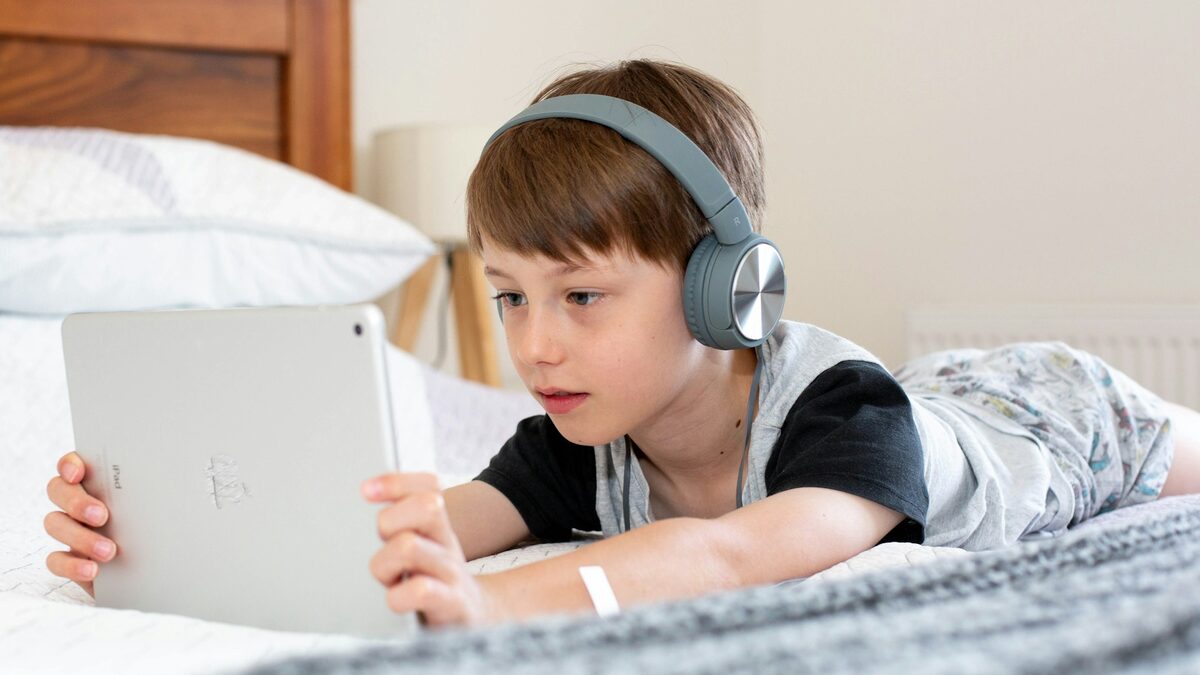 Elev cu căști care citește pe tabletă ce înseamnă GPT, întins pe pat
