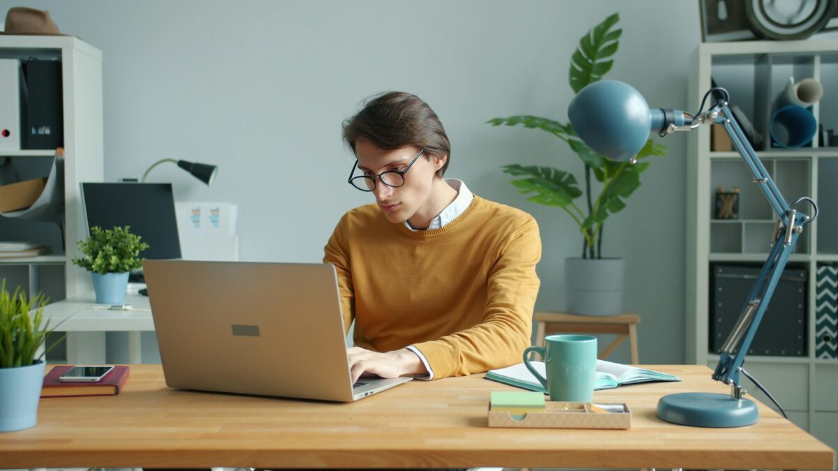 Tânăr la birou care citește pe laptop cum funcționează ChatGPT, cu un caiet de notițe alături