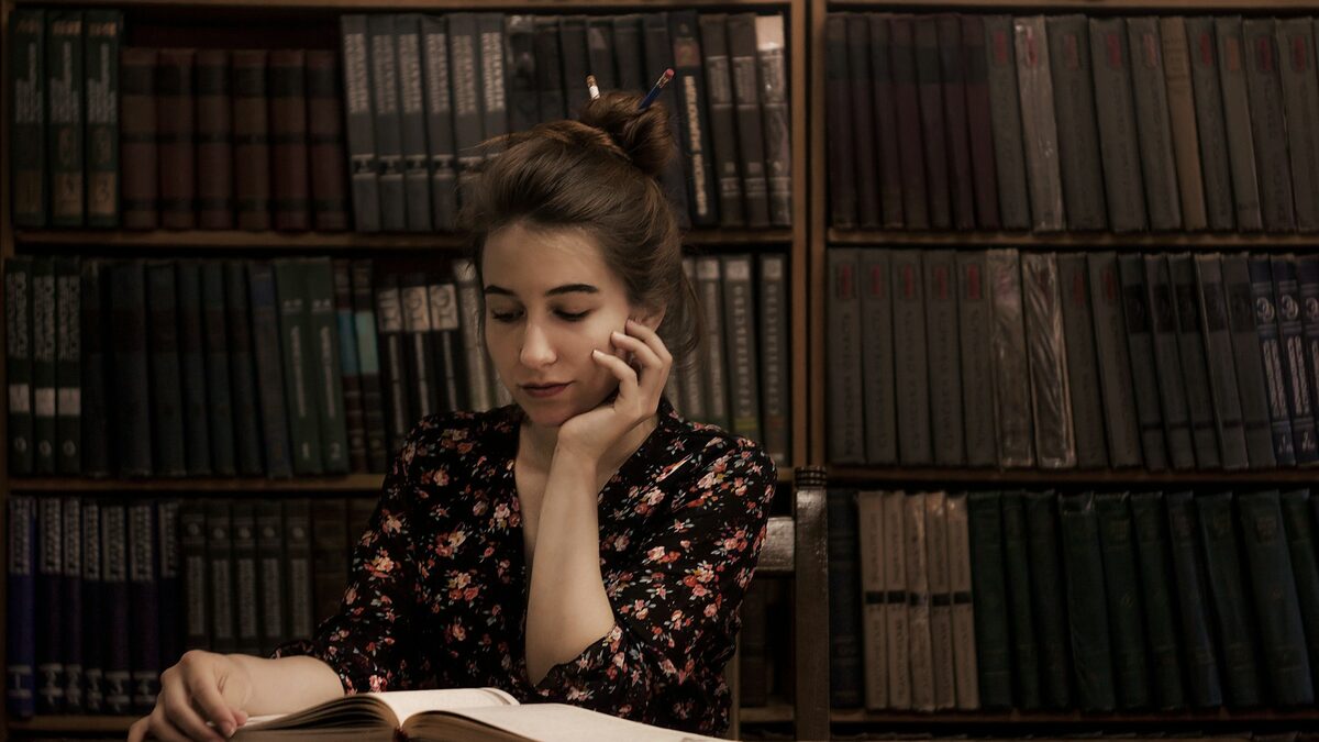 Tânără la bibliotecă care verifică într-o carte o informație, după ce a aflat despre halucinațiile AI