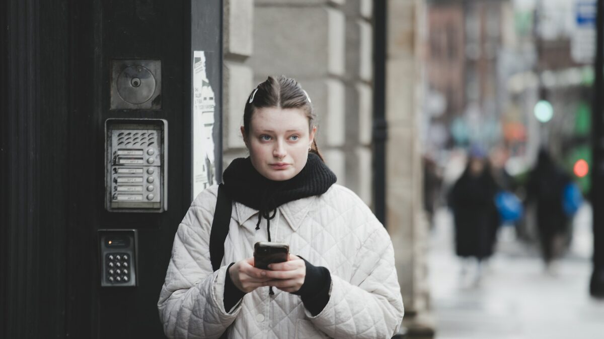 Femeie în fața interfonului blocului, care citește pe telefon mesajul că curierul nu te-a găsit acasă