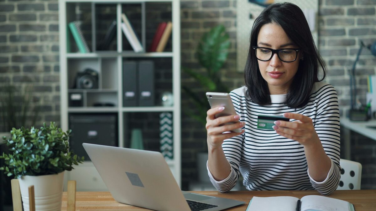 Femeie care plasează prima comandă online pe telefon, cu cardul bancar în mână