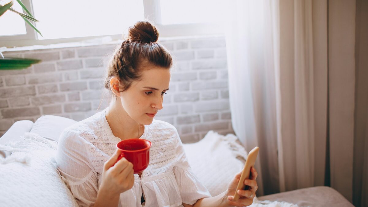 Femeie care citește știri pe telefon cu o cană de ceai în mână, gestionând calm anxietatea legată de AI