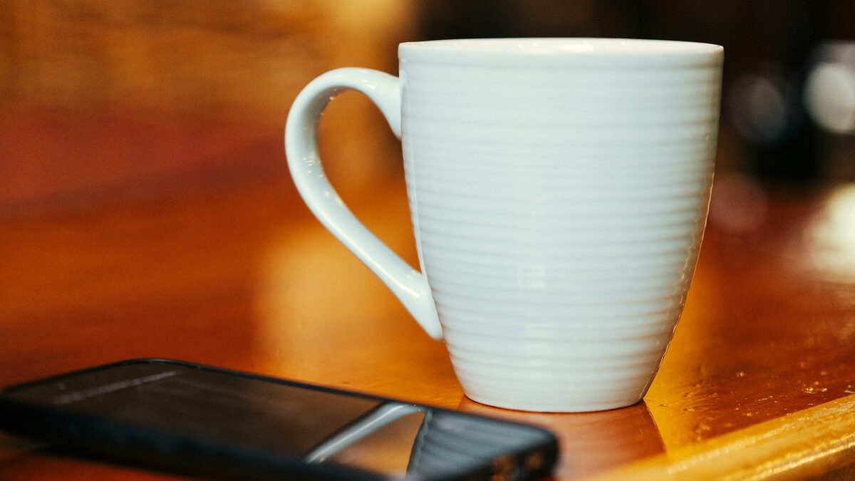 Telefon lăsat deoparte lângă o cană de cafea, exemplu simplu de folosire sănătoasă a AI