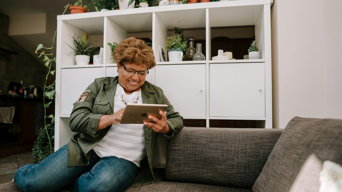 Femeie în vârstă, pe canapea, care vorbește pe tabletă cu un prieten virtual AI