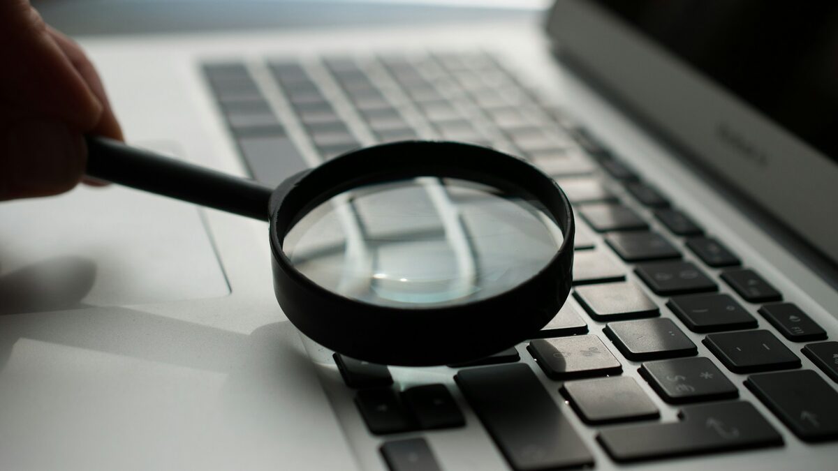 Lupă ținută deasupra tastaturii unui laptop, ca imagine pentru ce este SEO explicat simplu: cum te găsesc clienții în căutări