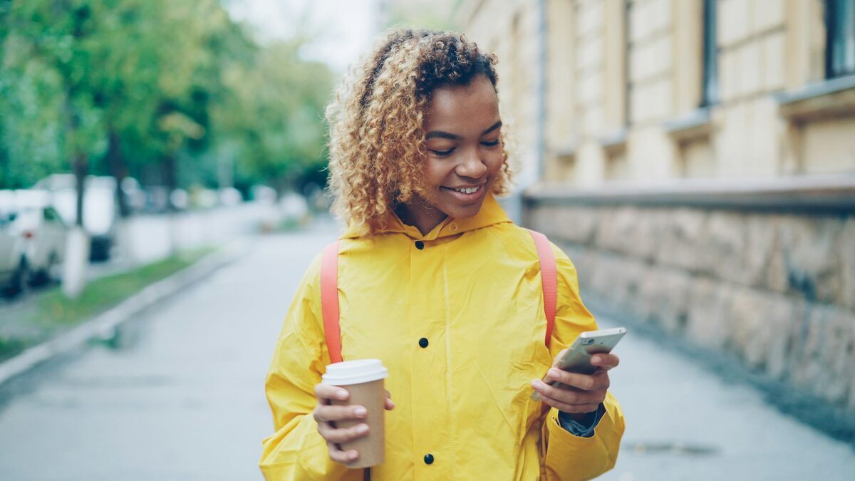 Tânără pe stradă care caută pe telefon un local apropiat, așa cum apari la căutările lângă mine