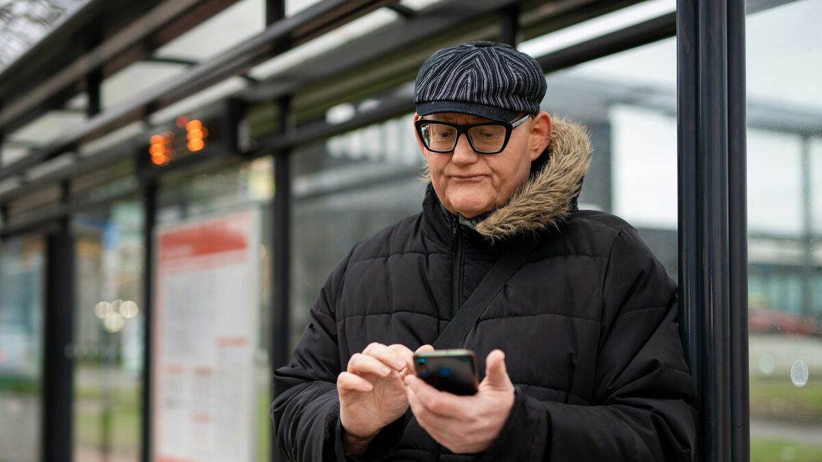 Bunic la stația de autobuz care folosește un smartphone, după ani în care a avut telefon cu butoane