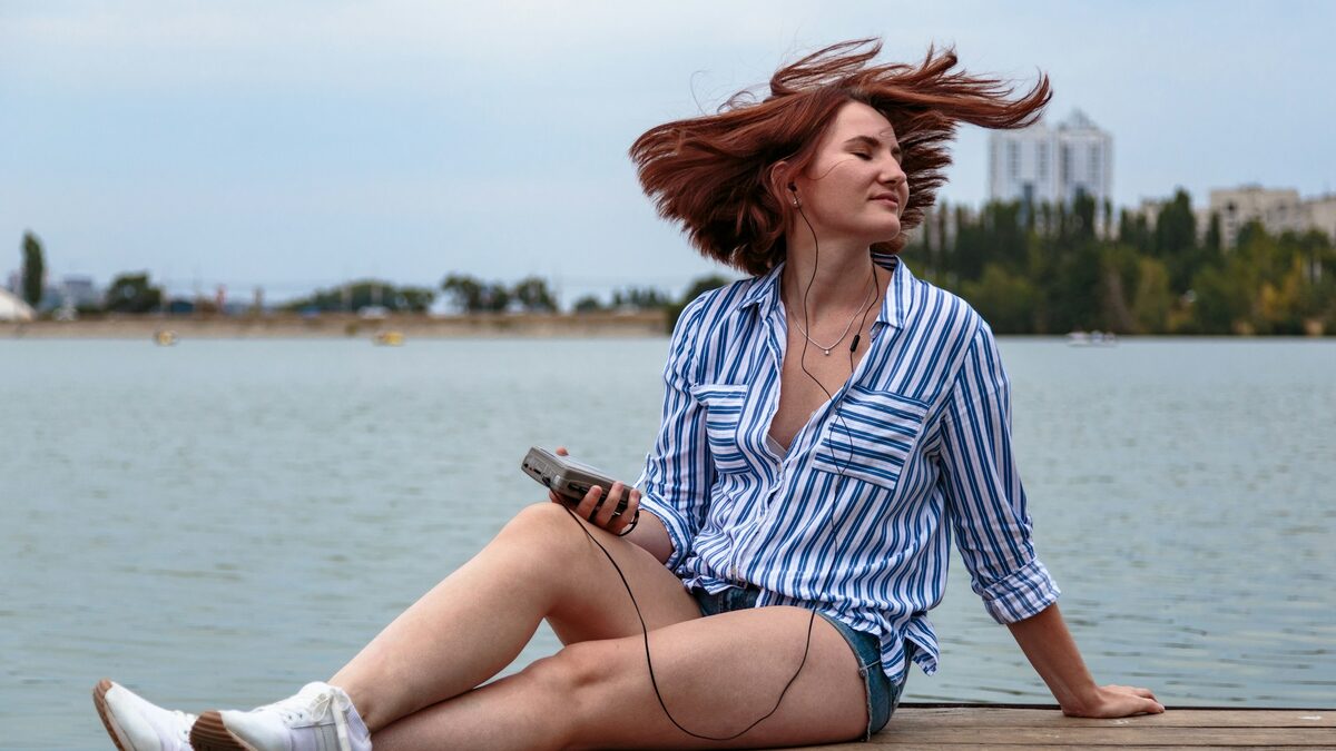 Femeie pe un ponton, cu căști în urechi, care folosește aplicații pentru învățat limbi străine pe telefon