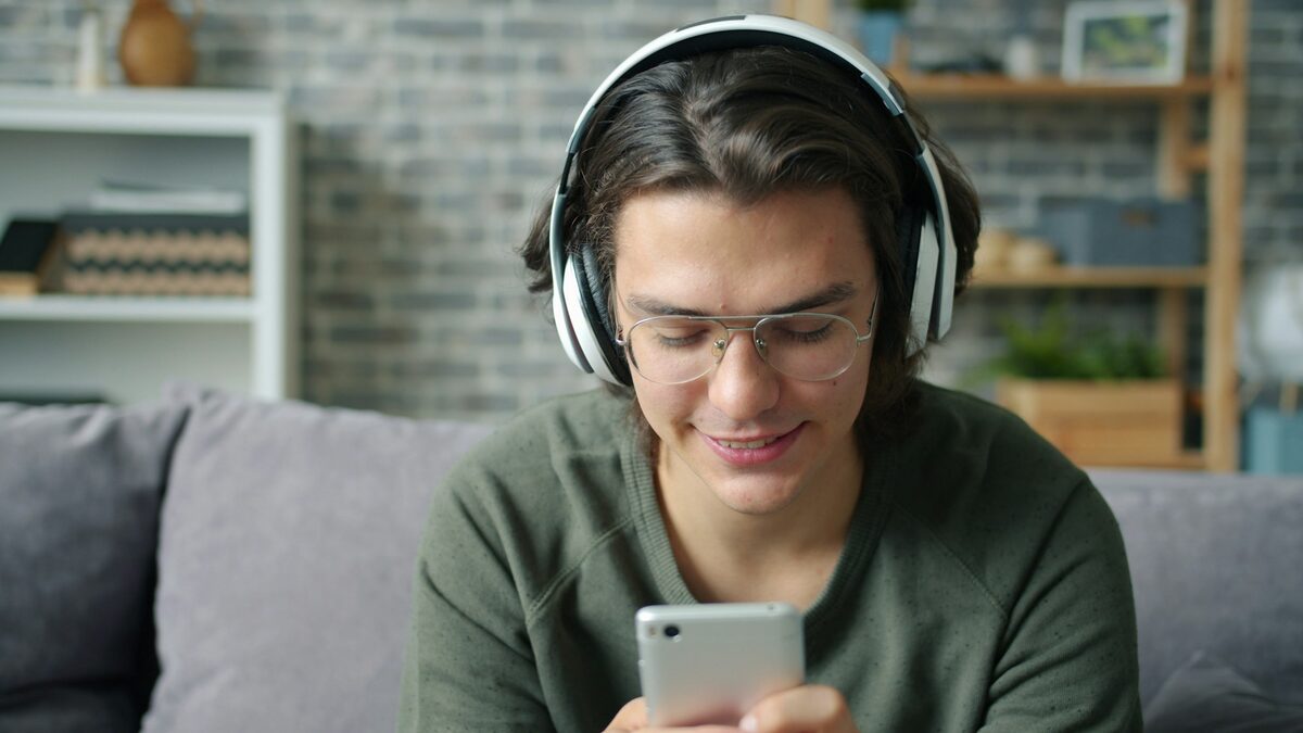 Tânăr cu căști care exersează pronunția corectă în engleză cu o aplicație AI pe telefon