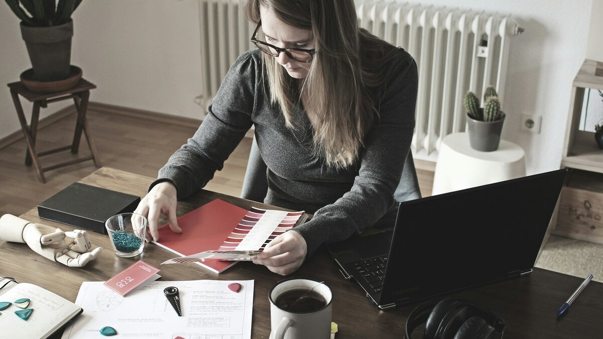 Femeie la birou care învață vocabular în limba germană cu fișe de hârtie, notițe și un asistent AI pe laptop