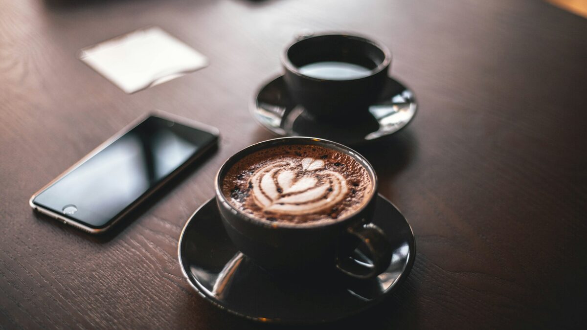 Telefon lăsat pe masa unei cafenele, lângă două cești de cafea, în timpul unei discuții despre dacă telefonul te ascultă