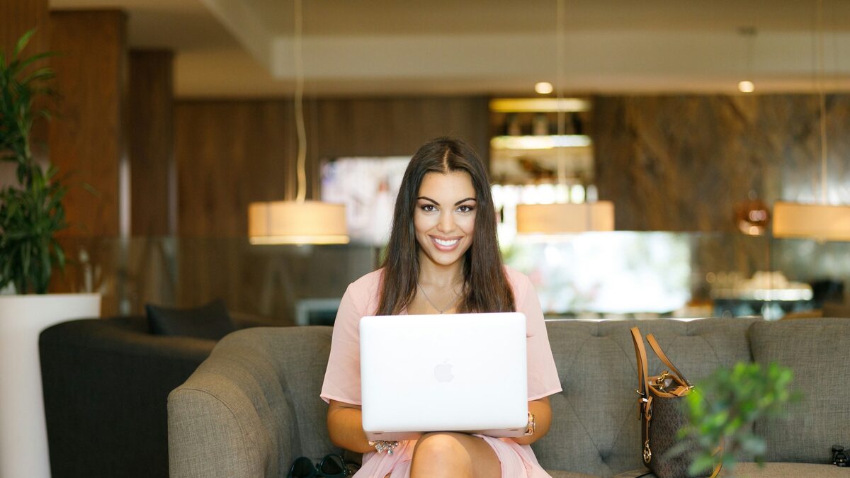Tânără pe canapea, cu laptopul pe genunchi, care își actualizează profilul de LinkedIn