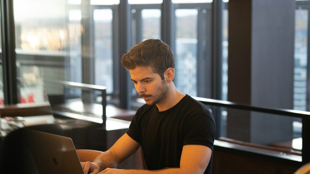 Bărbat tânăr într-o cafenea care își pregătește CV-ul pe laptop pentru sezonul de recrutări