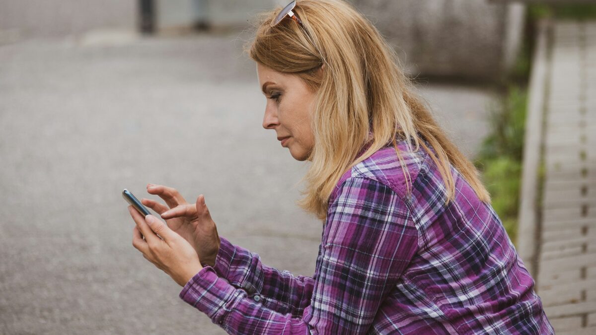 Femeie care mărește pe telefon o fotografie suspectă ca să verifice dacă e una dintre pozele false făcute cu AI