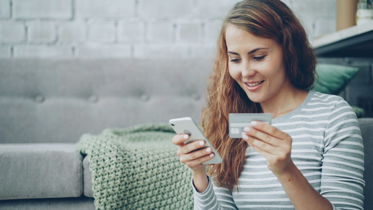 Femeie cu telefonul și cardul în mână care citește un SMS despre un colet și recunoaște țeapa cu coletul