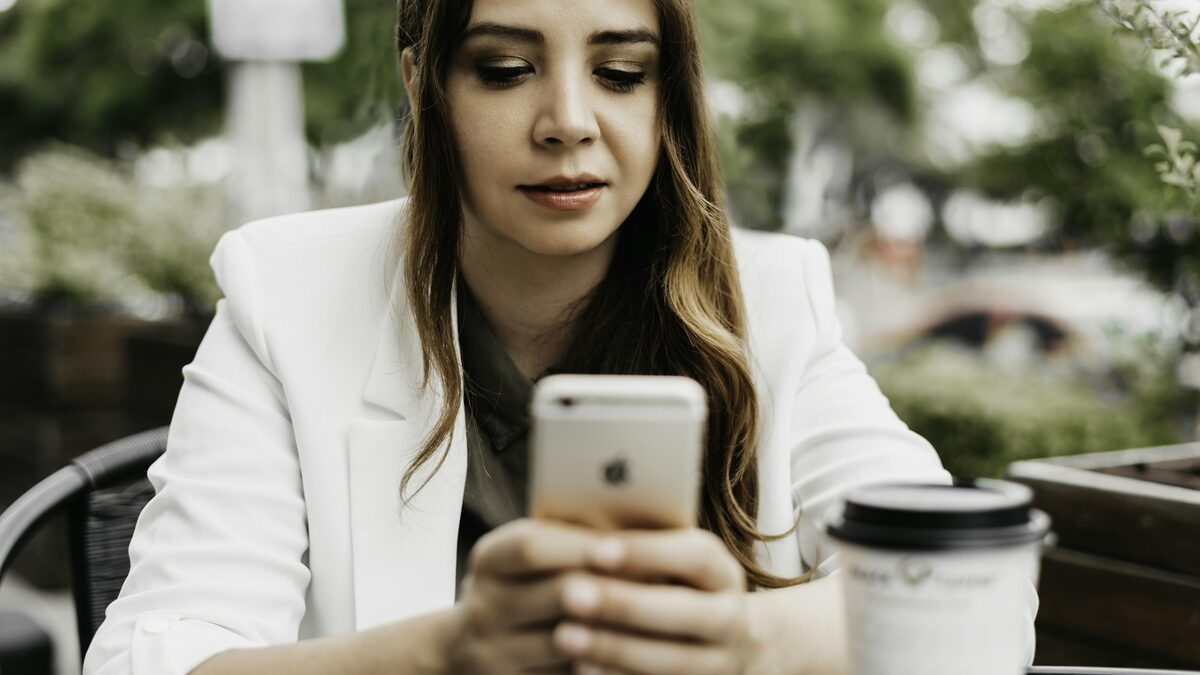 Femeie la o cafenea care verifică pe iPhone setările pentru a-și ține contul Apple în siguranță