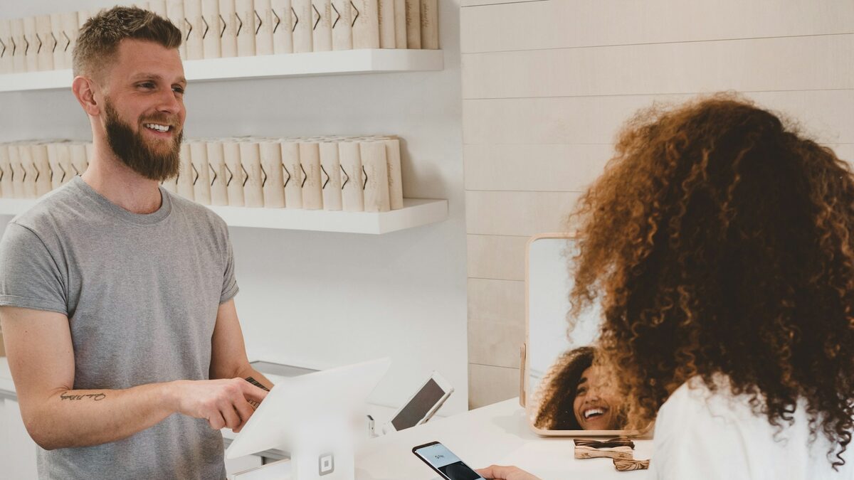 Clientă care plătește cu telefonul la un magazin mic, rapid și simplu, așa cum se așteaptă clienții și de la site în 2026
