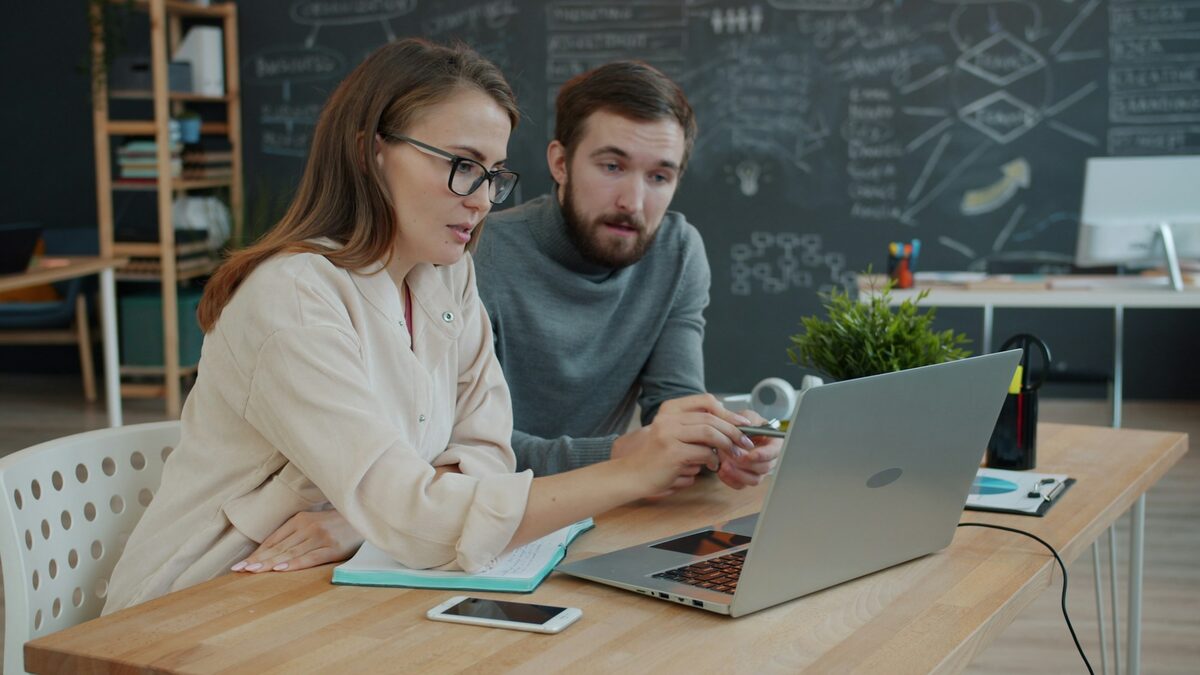 Doi asociați care compară la laptop dacă aleg un site simplu, inteligent sau autonom pentru firma lor