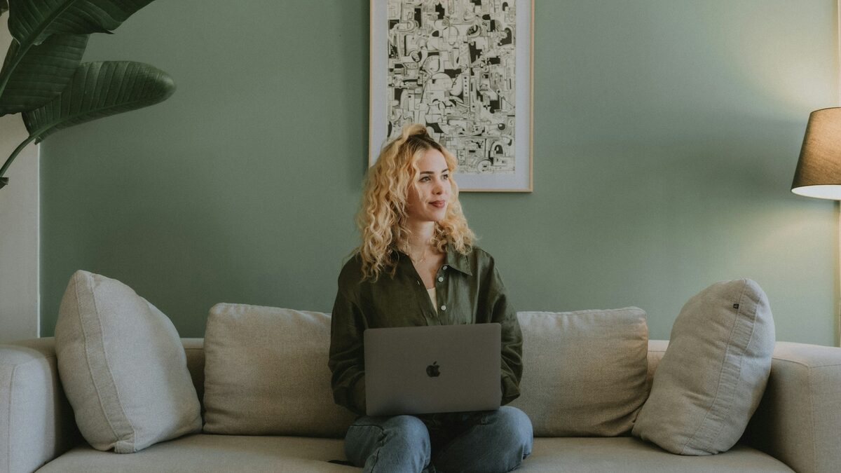 Femeie pe canapea cu laptopul în brațe, care așteaptă să se încarce o pagină pentru că internetul merge greu