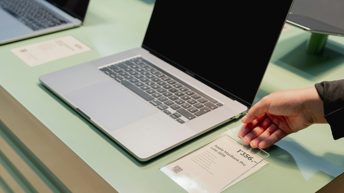 Mână care citește eticheta de preț a unui laptop în magazin, pentru a alege laptopul potrivit