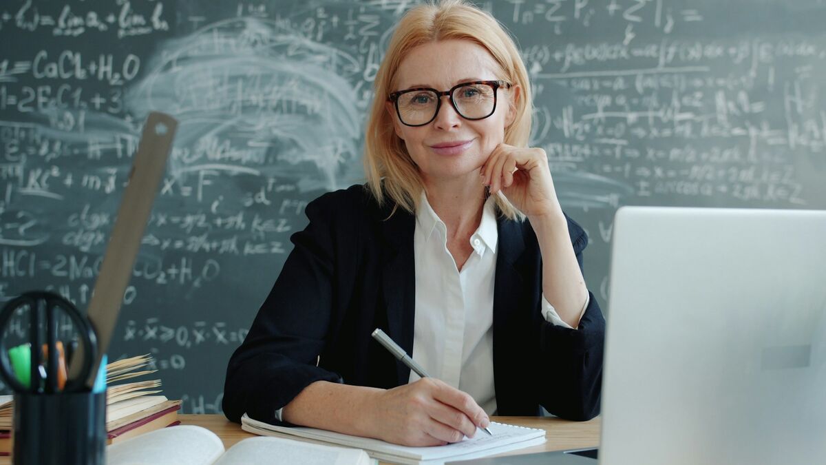Profesoară zâmbitoare la catedră, cu laptopul și notițele, care folosește AI pentru profesori și formatori