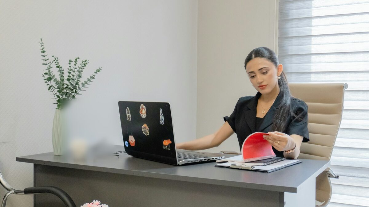 Femeie la birou care răsfoiește un dosar lângă laptop, ca să vadă cum sunt documente lungi citite repede cu AI
