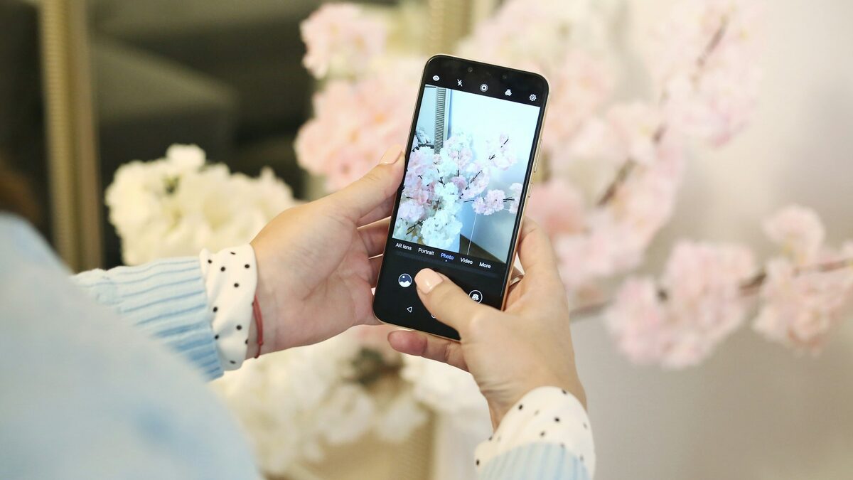 Mâini care fotografiază cu telefonul flori de primăvară, pentru postări pe Facebook și Instagram scrise cu AI